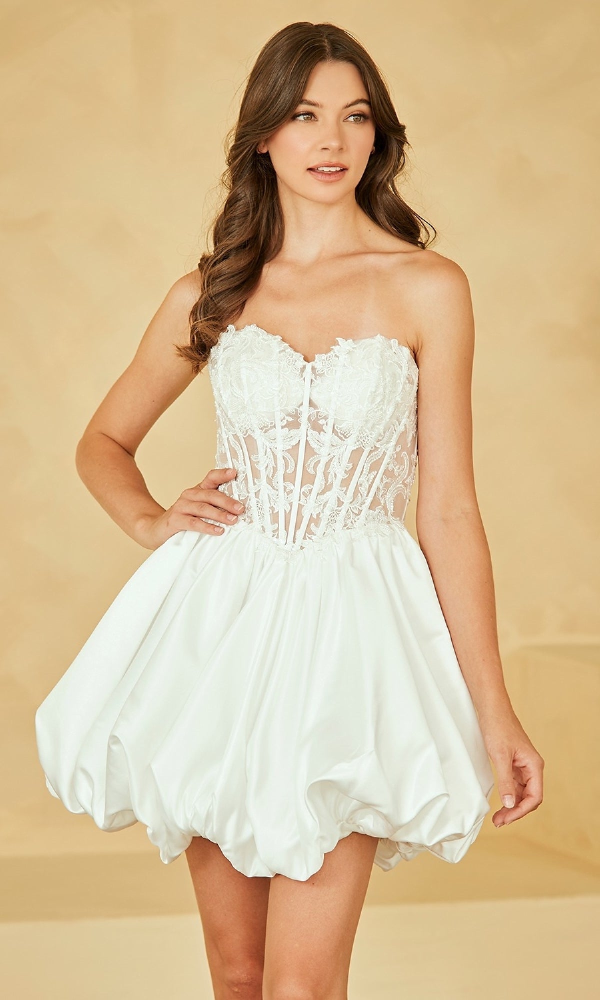 Woman wearing a short white strapless dress with a bubble hemline against a beige background